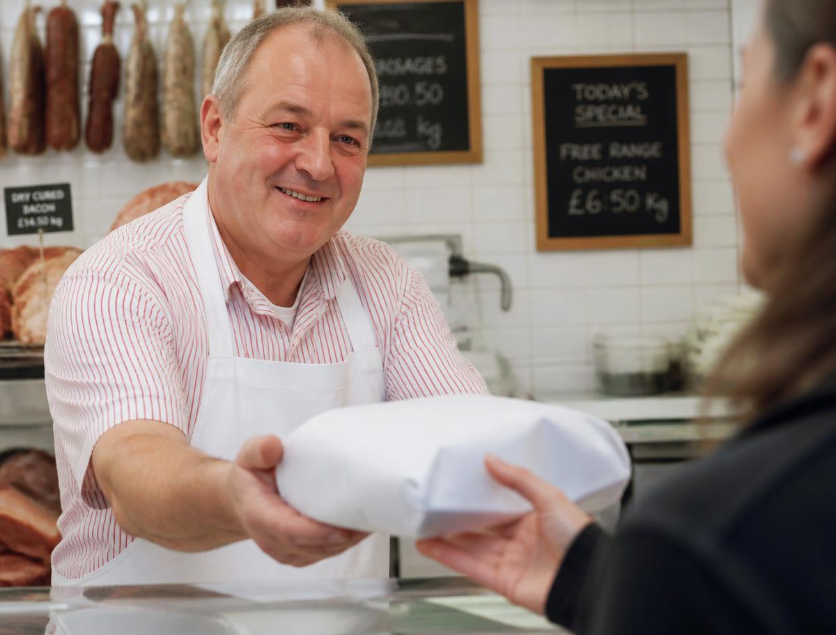 Butcher handing a wrapped parcel of fresh meat to a customer over the counter